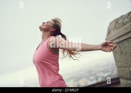 Nichts fühlt sich besser an als Fitness. Aufnahme einer glücklichen jungen Frau, die sich während eines Laufs in der Stadt frei fühlt. Stockfoto