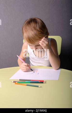 Ein kleiner Junge zeichnet mit Buntstiften am Tisch Stockfoto