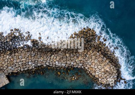 Luftdrohne von stürmischen windigen Wellen, die mit Macht das Wellenbrecher treffen. Extremes Wetter auf See. Stockfoto