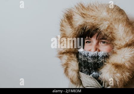 Junge trägt Wintermantel mit pelzigen Kapuze auf weißem Hintergrund. Stockfoto