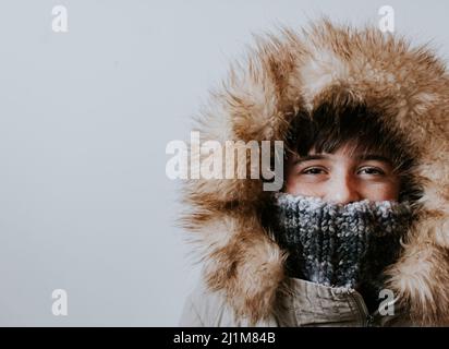 Junge trägt Wintermantel mit pelzigen Kapuze auf weißem Hintergrund. Stockfoto