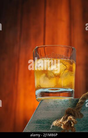 Ein Glas Whiskey mit Eis auf einem Ständer. Holzhintergrund. Alkoholisches Getränk. Moskau Russland 27. März 2022. Stockfoto