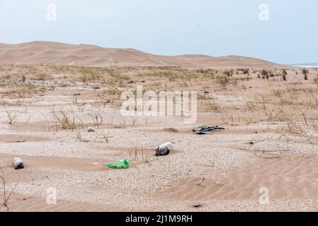 Plastikflaschen liegen auf dem Sand nahe dem Strand mit Dünen im Hintergrund. Konzept kümmern sich um die Erde. Stockfoto