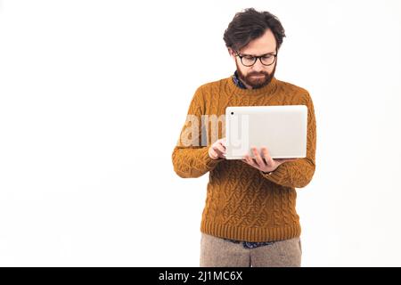 Medium shot junge gut aussehende bärtige konzentriert kaukasischen Mann stehend, mit seinem Laptop Blick auf den Bildschirm Hipster Remote Job Online-Lernkonzept weißen Hintergrund Kopie Raum isoliert Studio-Aufnahme . Hochwertige Fotos Stockfoto