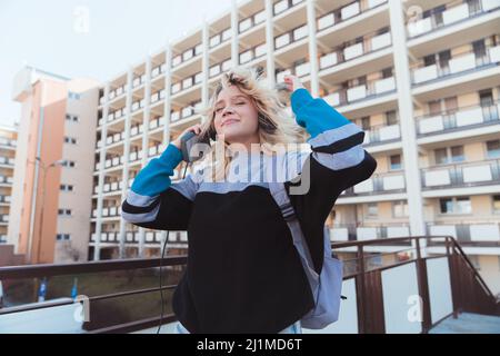 Verträumtes, glückliches kaukasisches Teenager-Mädchen mit Kassettenrecorder und Musik über altmodische Kopfhörer. Wohnblock im Hintergrund. Hochwertige Fotos Stockfoto