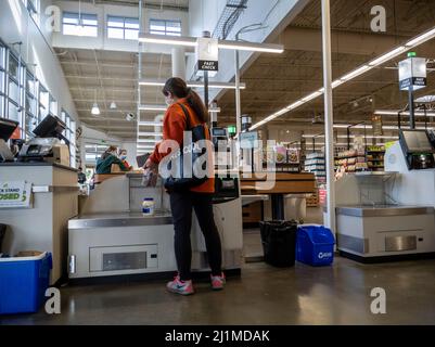 Lynnwood, WA USA - ca. März 2022: Blick auf eine Frau in einem roten Mantel, die im Self-Checkout-Bereich eines Stadt- und Landmarktes auscheckt Stockfoto