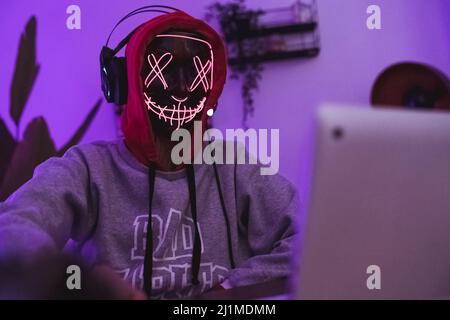 Professioneller Hacker in einer gruseligen Maske und roter Kapuze, der ein Verbrechen begeht. Internet- und Sicherheitskonzept. Hochwertige Fotos Stockfoto