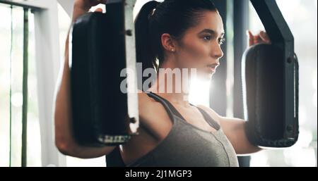 Sie wird nicht aufhören, bis sie dort ist. Eine kurze Aufnahme einer attraktiven jungen Sportlerin, die in einem Fitnessstudio mit einem Trainingsgerät trainiert. Stockfoto