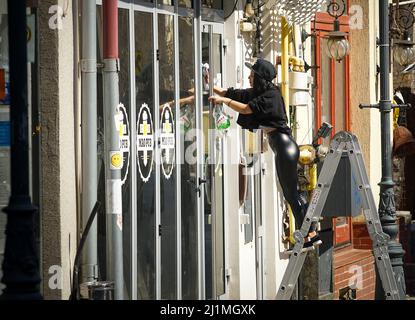 Bukarest, Rumänien - 24. März 2022: Eine junge Frau auf einer Leiter wäscht die Fenster einer Kneipe in der Altstadt von Bukarest. Stockfoto