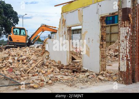 Ein kleines Geschäftsgebäude, das abgerissen wird. Ein Bagger steht auf einem Schutthaufen im Hintergrund Stockfoto