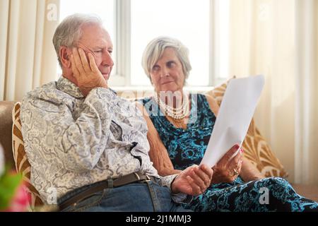 Weniger Einkommen, herausfordernde Ergebnisse. Aufnahme eines älteren Ehepaares, das zu Hause ihre Papiere durchläuft und besorgt aussieht. Stockfoto