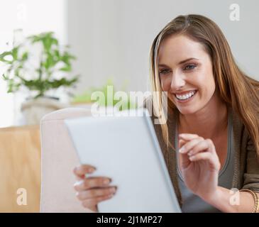 Aktualisierung ihrer sozialen Medien. Eine kurze Aufnahme einer attraktiven Frau, die sich mit ihrem digitalen Tablet auf dem Sofa zu Hause entspannt. Stockfoto