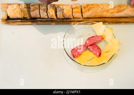 Draufsicht frisches und geschnittenes Baguette-Brot auf dem Tisch, um den Nachmittagssnack mit Käse und Wurst auf einer Glasplatte zuzubereiten, Essen für Partys und Stockfoto