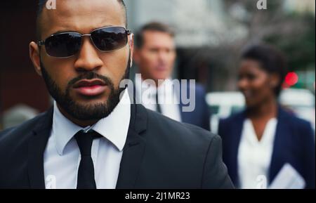 Nur ein weiterer Mann auf einer Mission. Aufnahme eines hübschen jungen Geschäftsmannes, der im Hintergrund mit seinen Kollegen in der Stadt unterwegs ist. Stockfoto