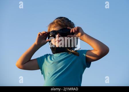 Kleiner Junge mit Pilotenbrille und Helm, Junge will Pilot und Astronaut werden. Glückliches Kind spielt am Himmel. Kinderpilot träumt vom Fliegen. Stockfoto