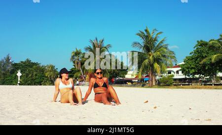 Zwei kaukasische hübsche Frauen im Bikini, die an einem Sandstrand sitzen, Koh Samui, Thailand Stockfoto