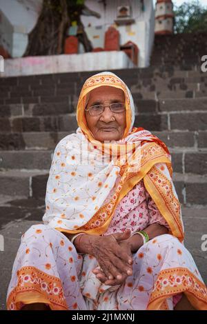 Eine ältere indische Witwe, eine Hindu, sitzt auf den Stufen des Banganga Tanks, einer heiligen Hindu-Stätte im Walkeshwar-Gebiet in Mumbai, Indien Stockfoto