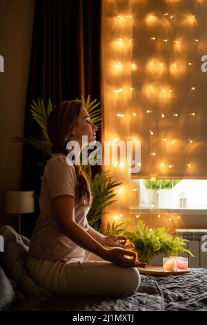Entspannte Yoga-Frauenmeditation in Lotusposition mit Handnamen auf dem Bett im Schlafzimmer Stockfoto