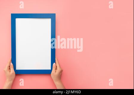 Frau halten leere Diplomrahmen auf rosa Wand Hintergrund. Weibliche Hände halten einen leeren Mockup-Rahmen. Beschnittene Hand einer Frau, die den Bilderrahmen gegen Rosa hält Stockfoto