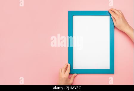 Frau halten leere Diplomrahmen auf rosa Wand Hintergrund. Hängender Fotorahmen-Nachbau an rosa Wänden. Bild-Frame-Modell. Halterahmen. Weibliche Hände Hol Stockfoto