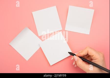 Haftnotizpapier zum Nachbau. Handgeschriebene Notizen schwarzer Bleistift auf weißem Aufkleber.rosa Hintergrund.Frau Hand Schreiben auf weißen Haftnotizen. Geschäftsleute m Stockfoto