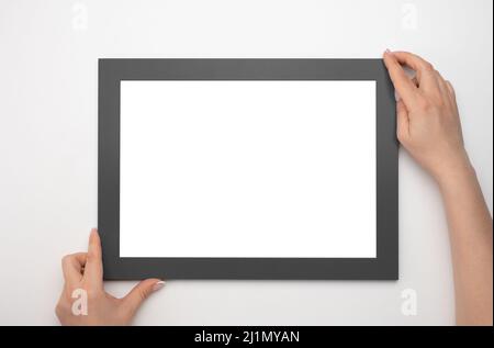 Nachbau des Haltrahmens. Foto-Mockup. Frau Hände halten schwarzen Rahmen. Für Rahmen- und Poster-Design. Rahmengröße A4. Isoliert auf weißem Hintergrund. Blank ph Stockfoto