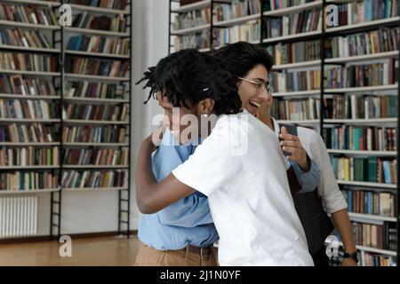 Glückliche multiethnische Teenager Studenten umarmen stehen in der Bibliothek Stockfoto