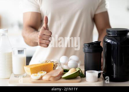 Nicht erkennbarer sportlicher Mann, der Daumen nach oben zeigt und eine gesunde Ernährung für Muskelaufbau oder Gewichtsverlust in der Küche empfiehlt Stockfoto