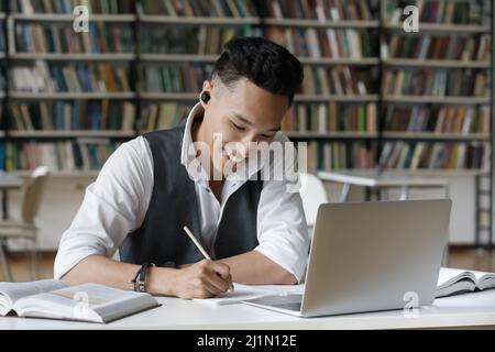 Asian Kerl nehmen Notizen im Copybook während des Studiums in der Bibliothek Stockfoto