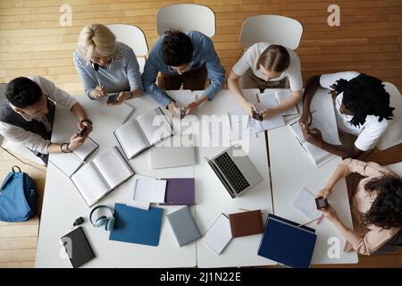 Ansicht von oben Multiethnische Studenten sitzen am Tisch und nutzen Smartphones Stockfoto