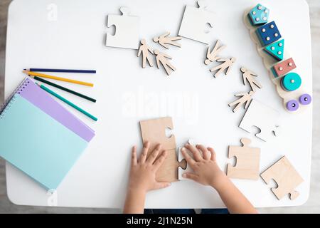 Unbekanntes kleines Kind, das mit Holzpuzzles auf dem Schreibtisch spielt, Draufsicht, freier Platz Stockfoto