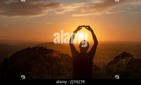 Silhouette eines Mannes, der die Arme hebt und die Sonne umarmt. Stockfoto