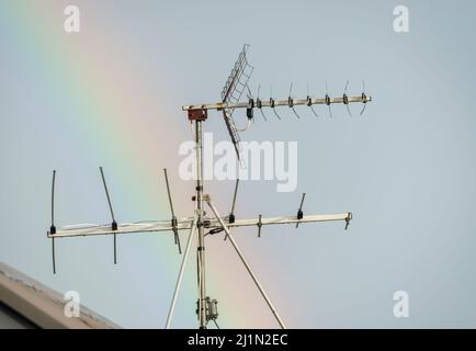 Fernsehantenne auf dem Dach eines Hauses, gegen einen Regenbogen über dem Himmel. Stockfoto