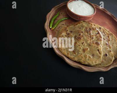 aloo Paratha mit Quark auf dem Teller serviert. Traditionelle nordindische Küche. Aufgenommen vor schwarzem Hintergrund. Stockfoto