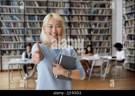 Asiatische Student Mädchen Pose in Bibliothek zeigt Daumen nach oben Zeichen Stockfoto