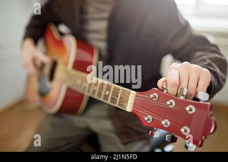 Nahaufnahme eines jungen Mannes, der sitzt und die Saiten der Gitarre stimmt, bevor er die Musik spielt Stockfoto