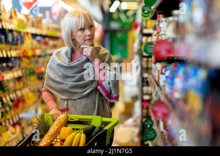 Verwirrte Kundin, die im Supermarkt auf das Regal mit Saucen schaute Stockfoto