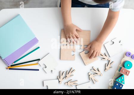 Draufsicht Hände des kleinen Kindes, die Holzpuzzles arrangieren, Symbol des öffentlichen Bewusstseins für Autismus-Spektrum-Störungen Stockfoto