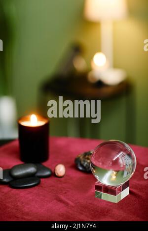 Vertikales Hintergrundbild von Kristallkugel und Kerzen auf rotem Samttisch im Wahrsagerladen, Kopierraum Stockfoto
