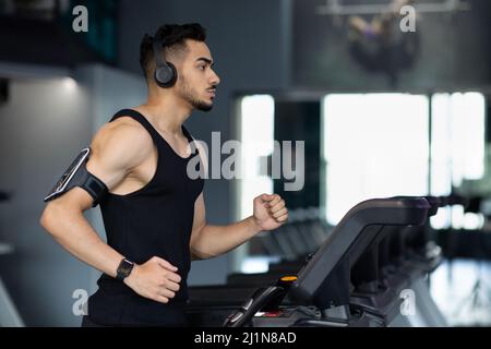 Muskulöser Arabischer Athlet Mit Kabellosen Kopfhörern, Der Auf Dem Laufband Im Fitnessstudio Läuft Stockfoto