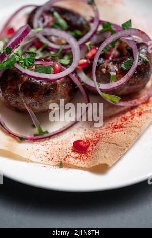 georgische gebratene Schweinefleischwürste kupaty mit Zwiebeln, Koriander auf Pita auf weißem Teller Stockfoto