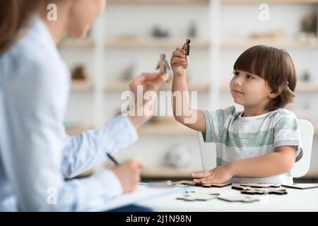 Kleiner Junge mit Kommunikationsprobleme, der mit Holzfiguren mit einem professionellen Kinderpsychologen im Büro spielt Stockfoto