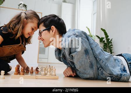 Spaß competitive Schach-Match zwischen Vater und seinem Kind Tochter. Mit dem Kopf schlagen, um Rivalen zu spielen. Seitenansicht. Auf dem Küchenboden. Stockfoto