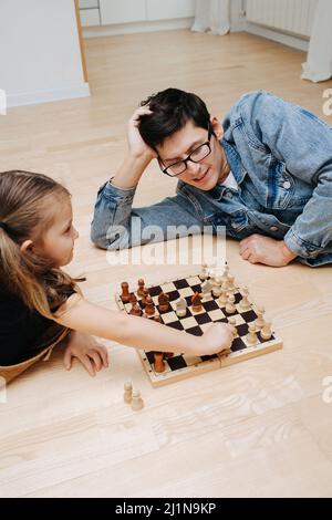 Freche Mädchen spielen Schach mit ihrem Vater. Sowohl aufgeregt und Spaß haben. Seitenansicht. Auf dem Küchenboden. Stockfoto