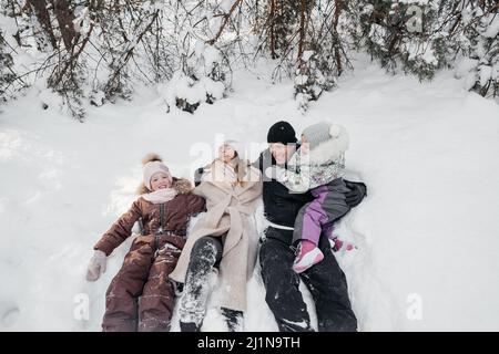 Vater, Mutter und Töchter liegen im Schnee im Winterwald Stockfoto