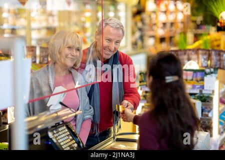 Fröhliches Ehepaar, das im Supermarkt mit Kreditkarte bezahlt hat Stockfoto