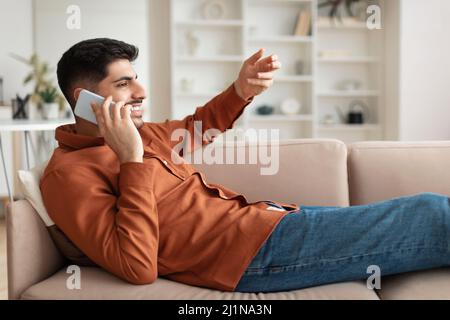 Profilportrait eines Mannes, der auf dem Mobiltelefon auf der Couch sitzt Stockfoto