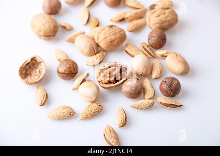 Verschiedene Nüsse in der Schale auf weißem Hintergrund: Walnüsse, Pekannüsse, Mandeln, Macadamia. Selektiver Fokus, Nahaufnahme. Stockfoto