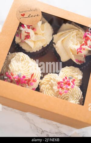 Verpacken Sie frisch gebackene Cupcakes aus rotem Samt mit weißer Schokolade-Ganache, die in die Cupcake-Box zuckert. Stockfoto