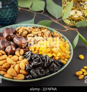 Ramadan-Konzept. Nüsse, getrocknete Früchte und Datteln in der blauen Schale, Glas Wasser und ramadan-Laterne auf schwarzem Hintergrund mit Kopierraum. Arabisches Gericht, s Stockfoto